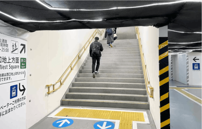 西口地上方面の案内板がある階段を上る